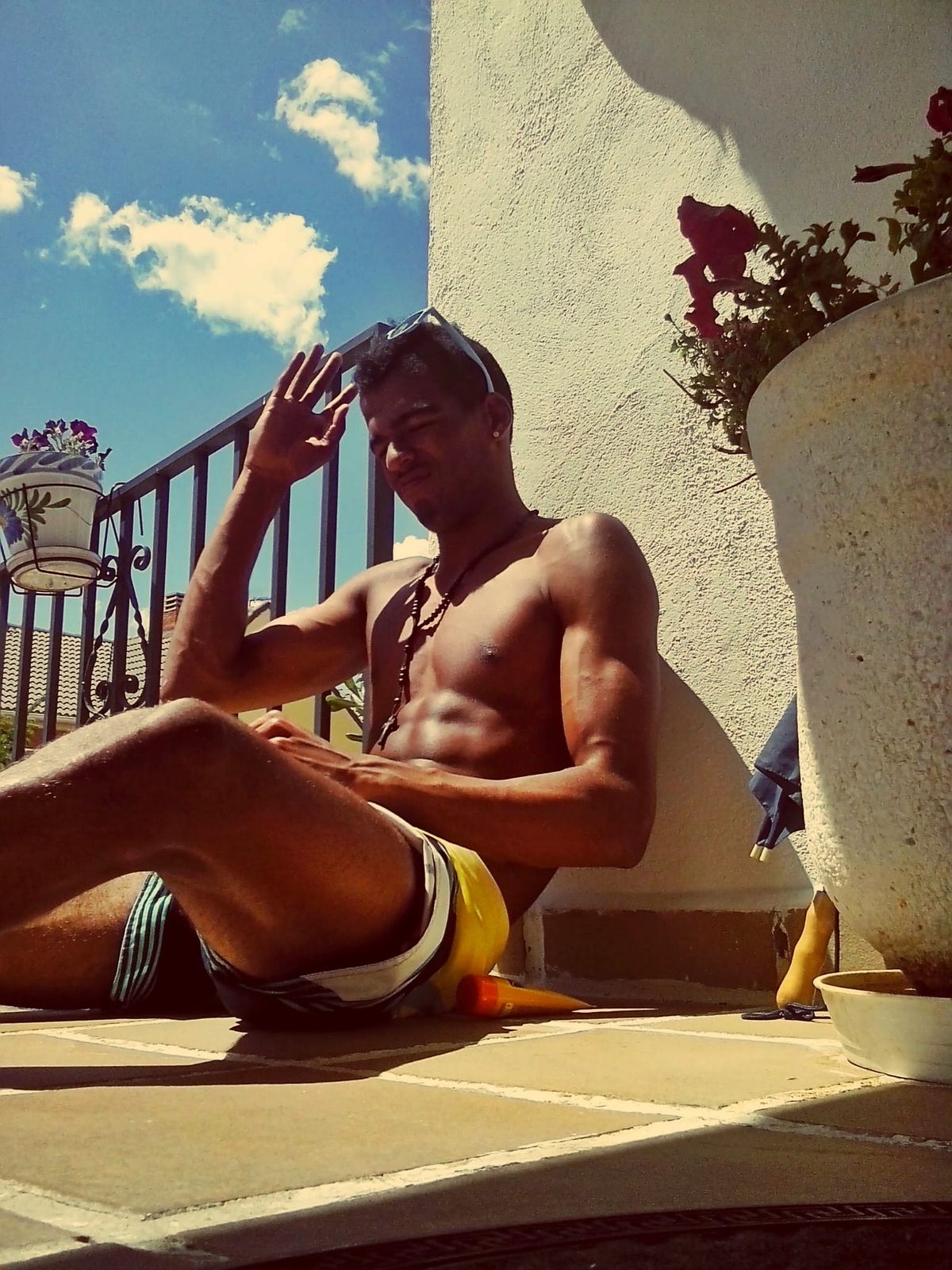 Manu sitting in the sun on a terrace, waving, the first change already visible