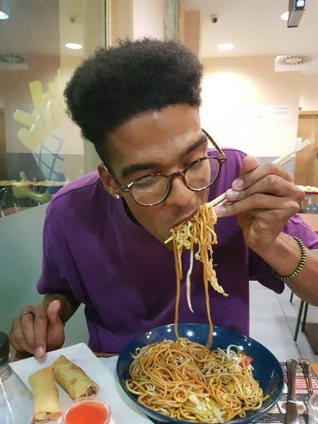 Manu, very skinny, eating a huge plate of noodles with chopsticks